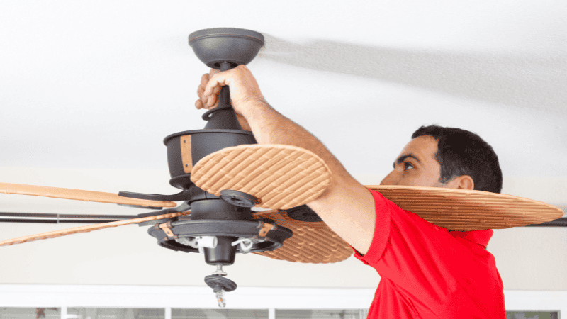 A person manually adjusting the direction switch of a ceiling fan. 