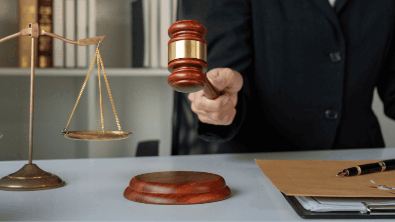 Человек стоит возле весов, готовый ударить молотком, показывая, что мы должны утилизировать использованные лампочки в соответствии с законом.