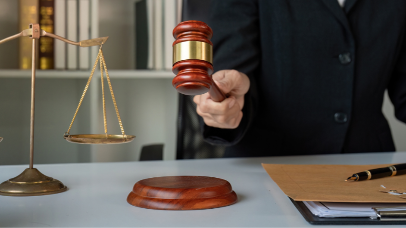 A person stands beside a balance, ready to strike the gavel, indicating that we should handle the used light bulbs legally.